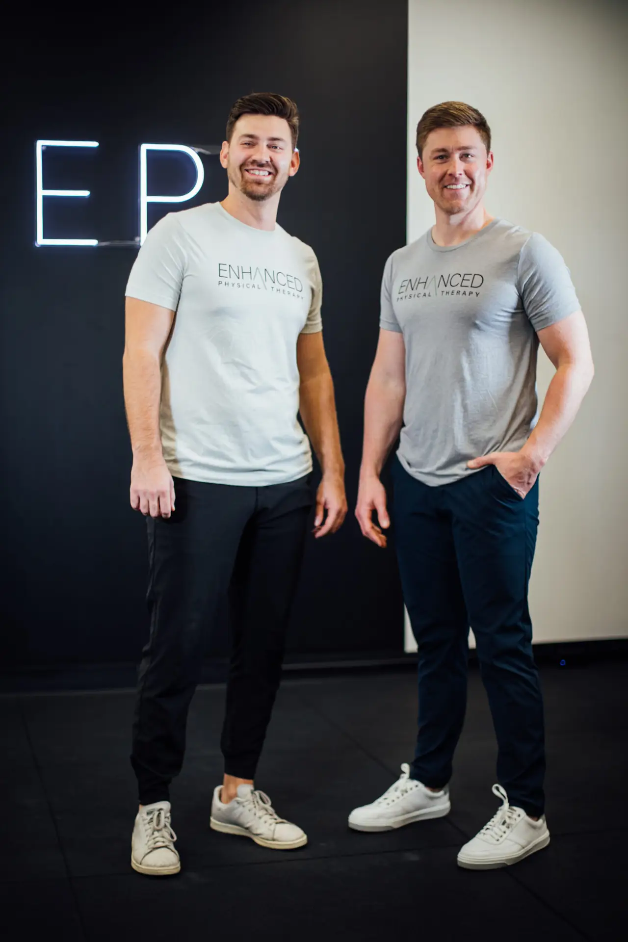 Josh Wilson and Zach White, founders of Enhanced Physical Therapy, in front of the EPT neon sign
