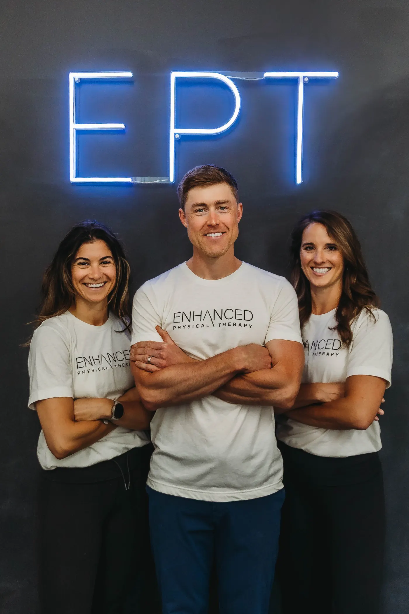 Zach White, Melissa McEnroe, and Gina Gapstur of Enhanced Physical Therapy in front of the EPT neon sign